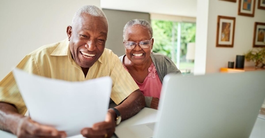 black retired couple on the computer and laughing while looking at a piece of paper