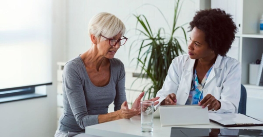older women with short grey hair talking to a black female doctor